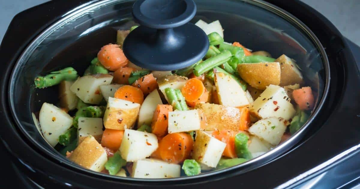 Close up view of slow cooker cooking a mix of diced potatoes, green beans and carrots.