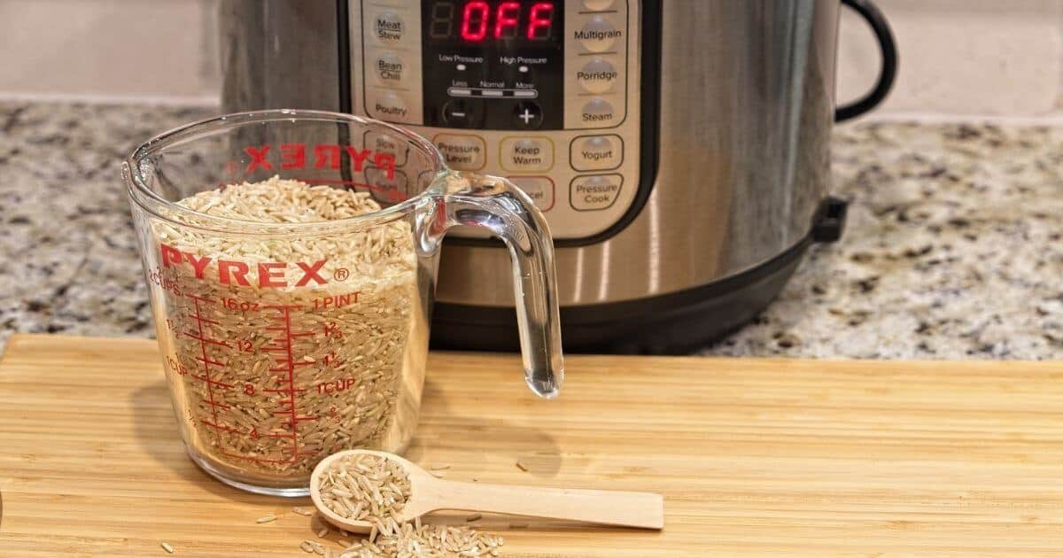 instant pot cooking on counter with measuring cup full of rice in front of it on a wooden cutting board.