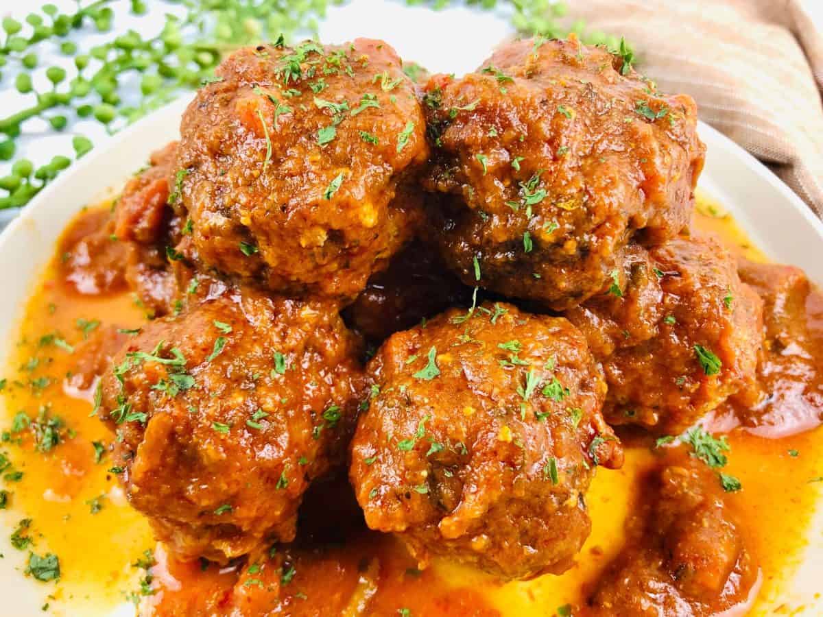 Close up view of white bowl filled with cooked gluten free sausage balls covered in sauce and herbs