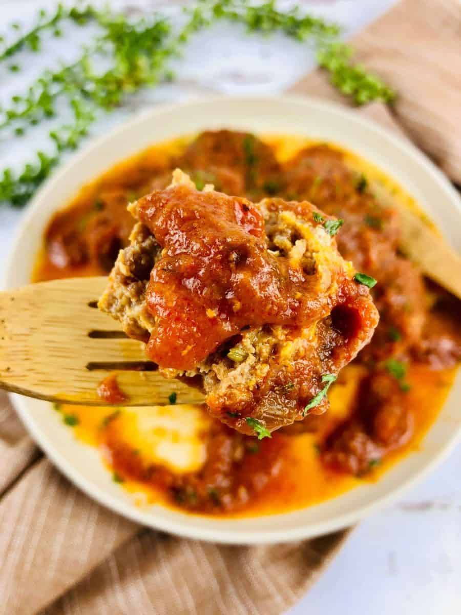 Close up vertical view of gluten free slow cooker meatballs with a wooden fork holding up one meatball