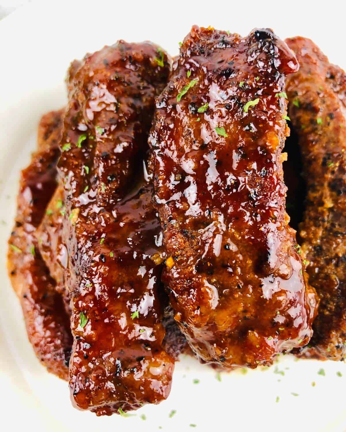 Cooked and sauced pork ribs on a white plate.