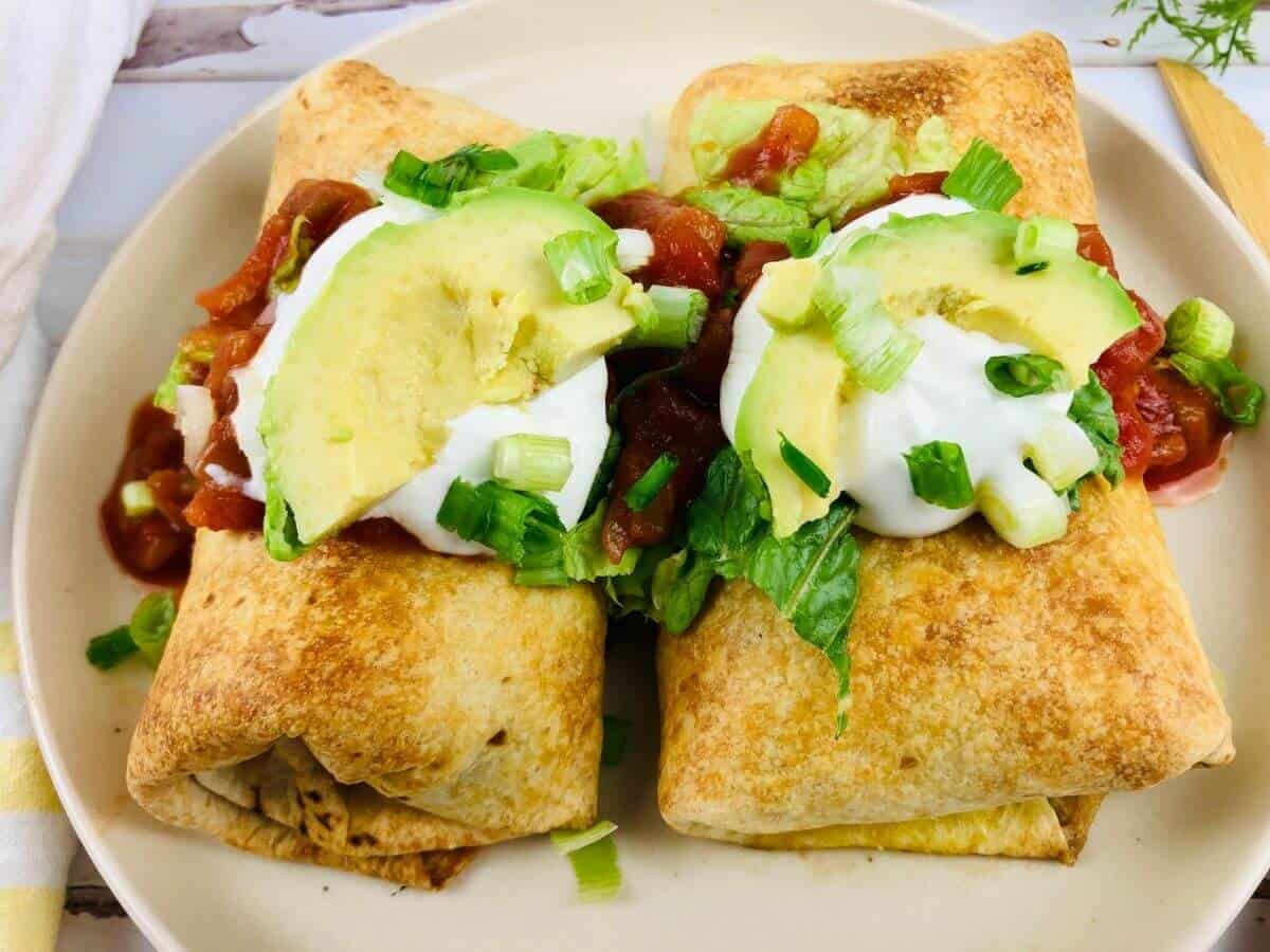 Two air fryer chimichangas on a plate loaded with toppings.