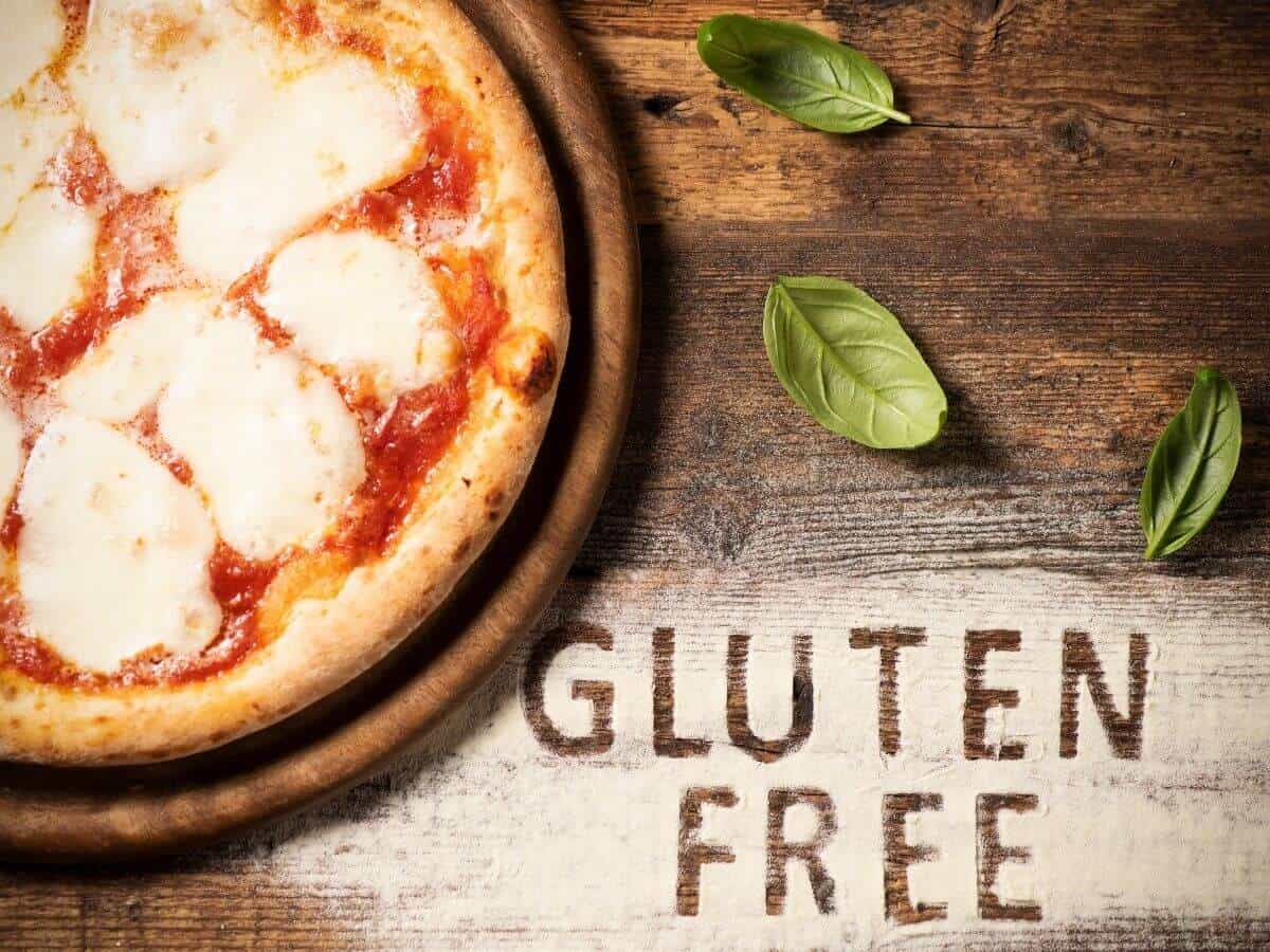 Gluten free pizza in the corner with basil on the side and "gluten free" written in flour on a wooden table.