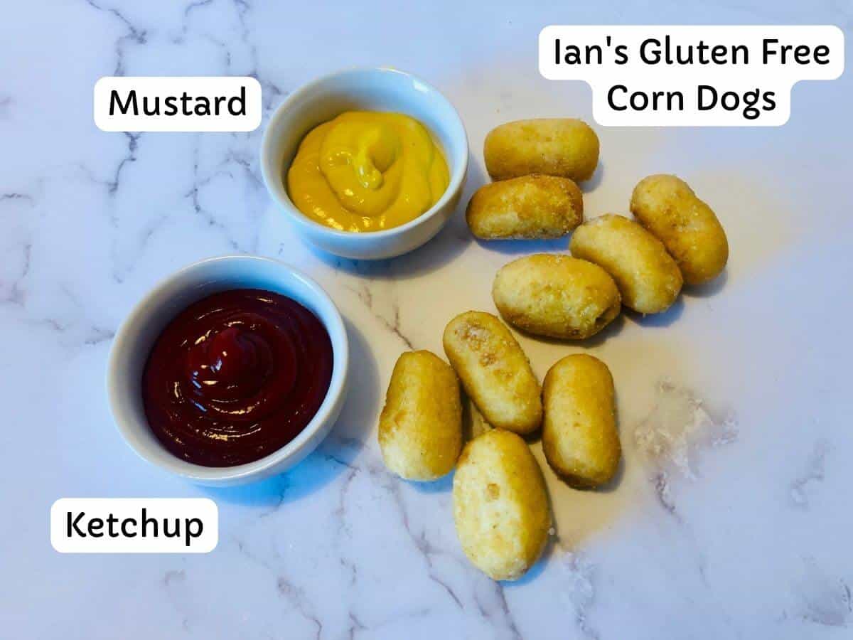 Mini corndogs on white marble surface with 2 filled dip containers on the side.