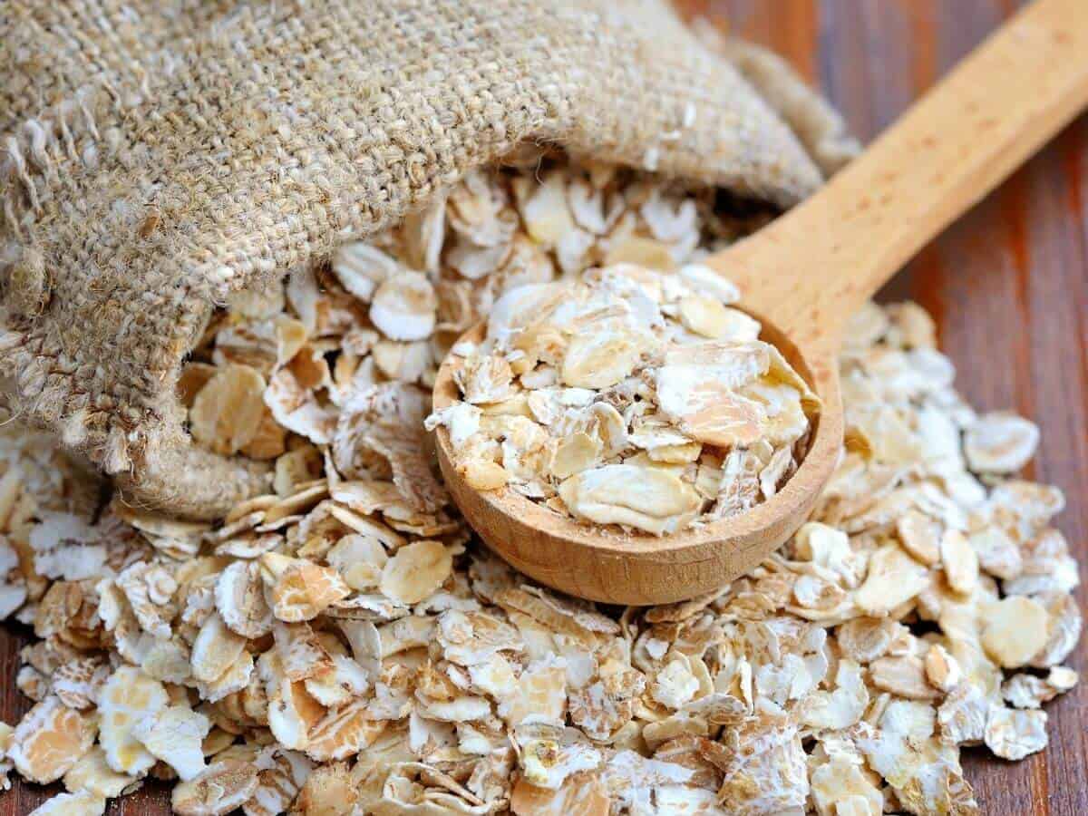 Oats on a a table being scooped up with a wooden spoon for the post: Is Couscous Gluten-Free?
