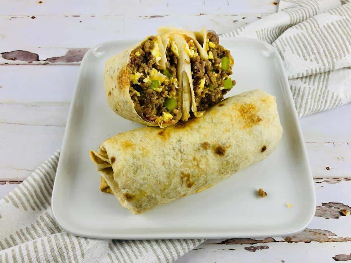 air fryer breakfast burritos cut and on a plate on top of a wooden table with a decorative napin.
