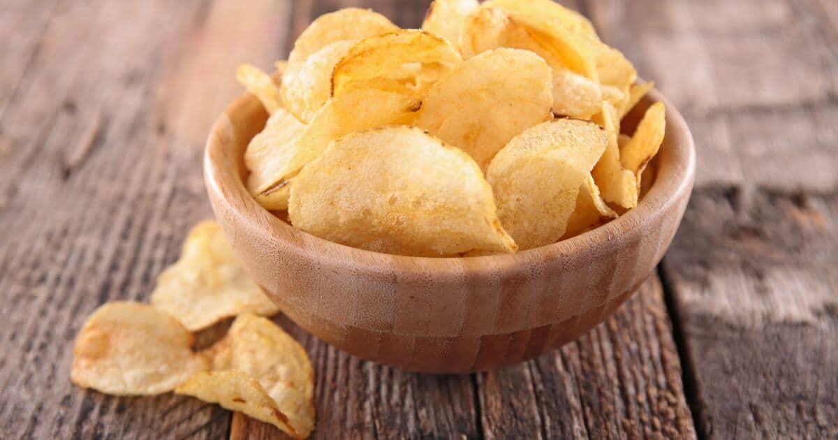 wooden bowl filled with potato chips on top of a wooden table.