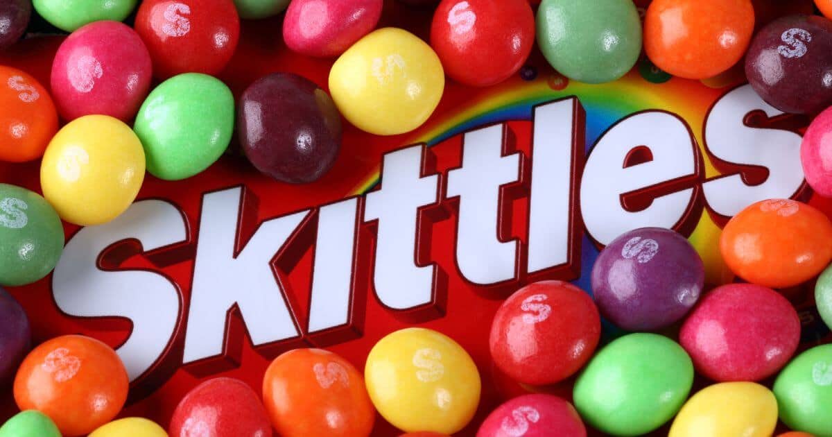 The Skittles logo surrounded by a lot of Skittles candies for the article titled: Are Skittles Gluten Free?