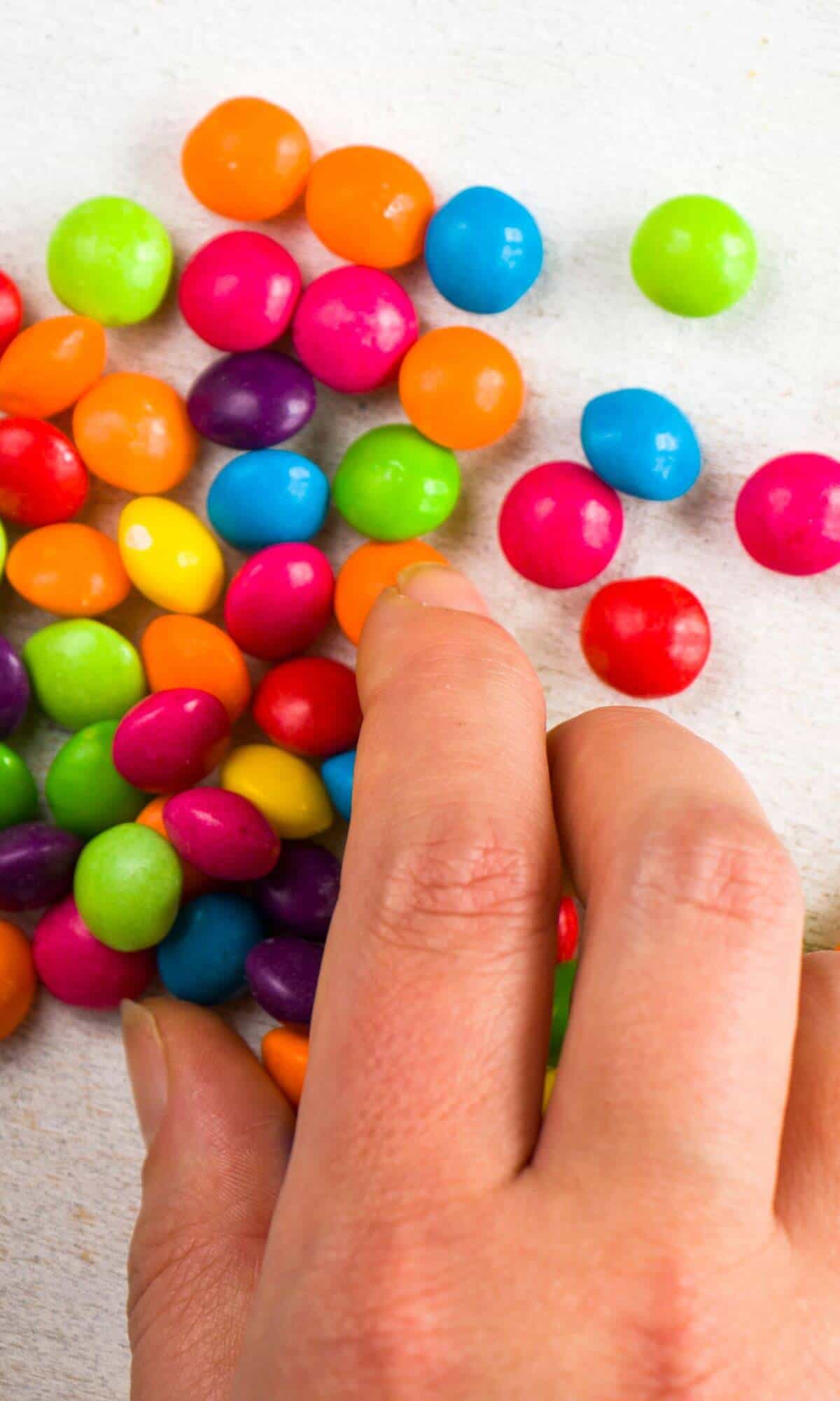 Hand touching a pile of Skittles candies for the article titled: Are Skittles Gluten Free?