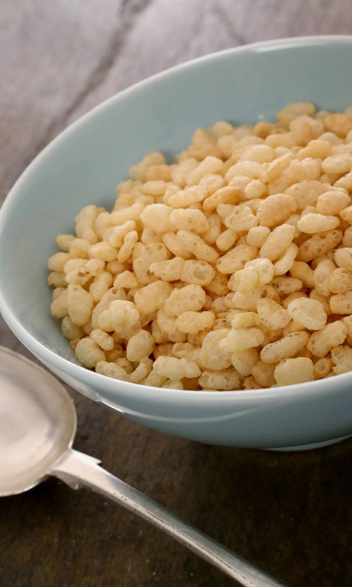A white bowl filled with rice cereal next to a spoon.