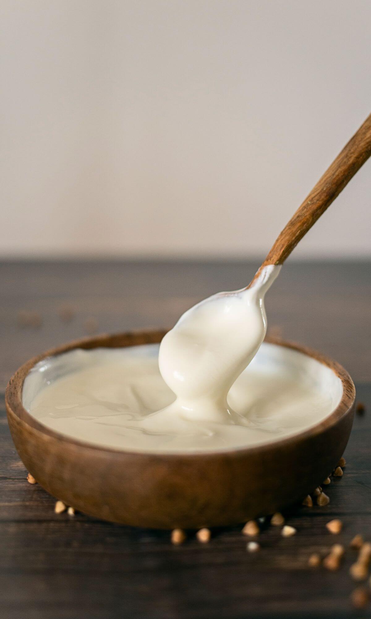 A wooden spoon dipping into a wooden bowl filled with sour cream.