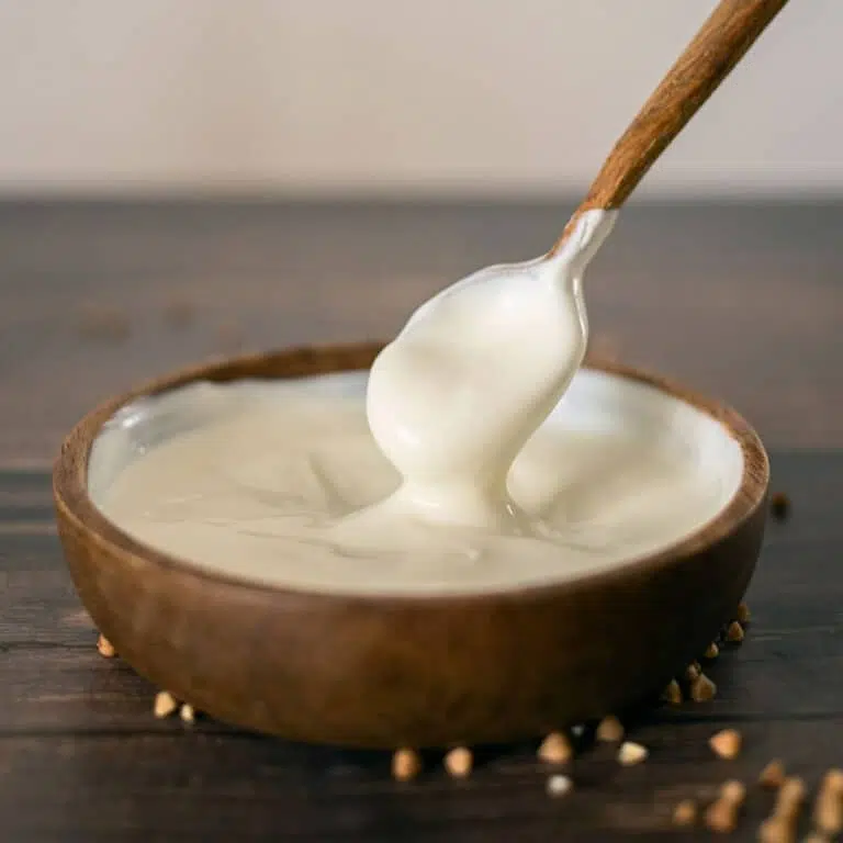 A wooden spoon dipping into a wooden bowl filled with sour cream.