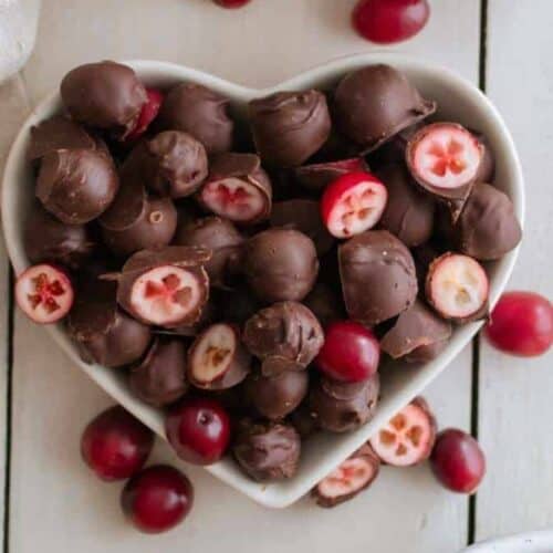 Chocolate covered cranberries in a white heart shaped bowl.