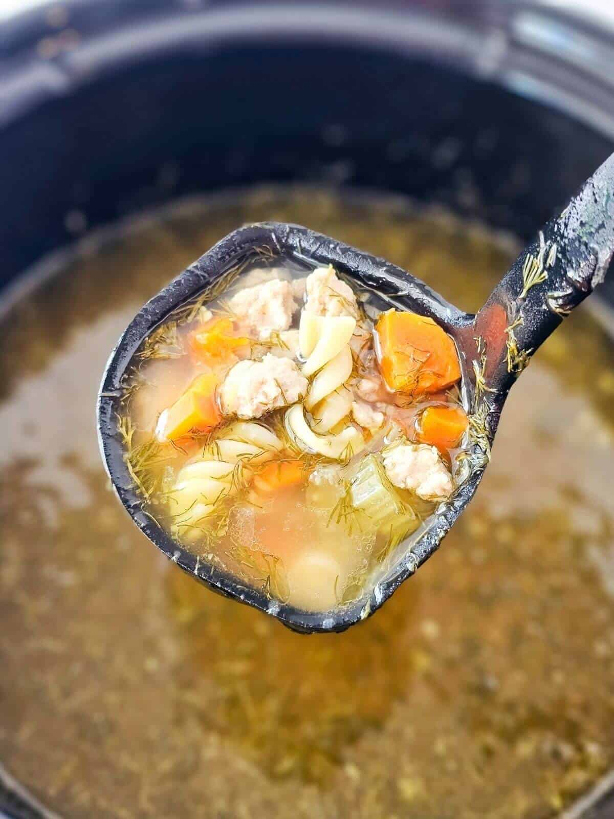 A ladle of soup being taken out of a slow cooker filled with ground chicken soup.