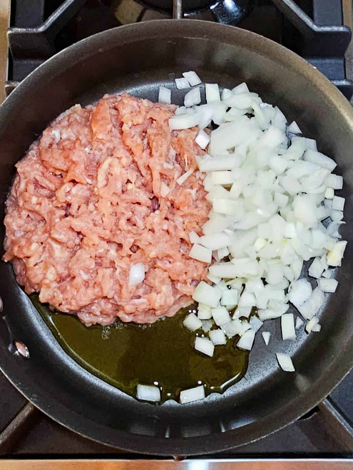 Raw ground chicken, olive oil and chopped onions in a skillet.