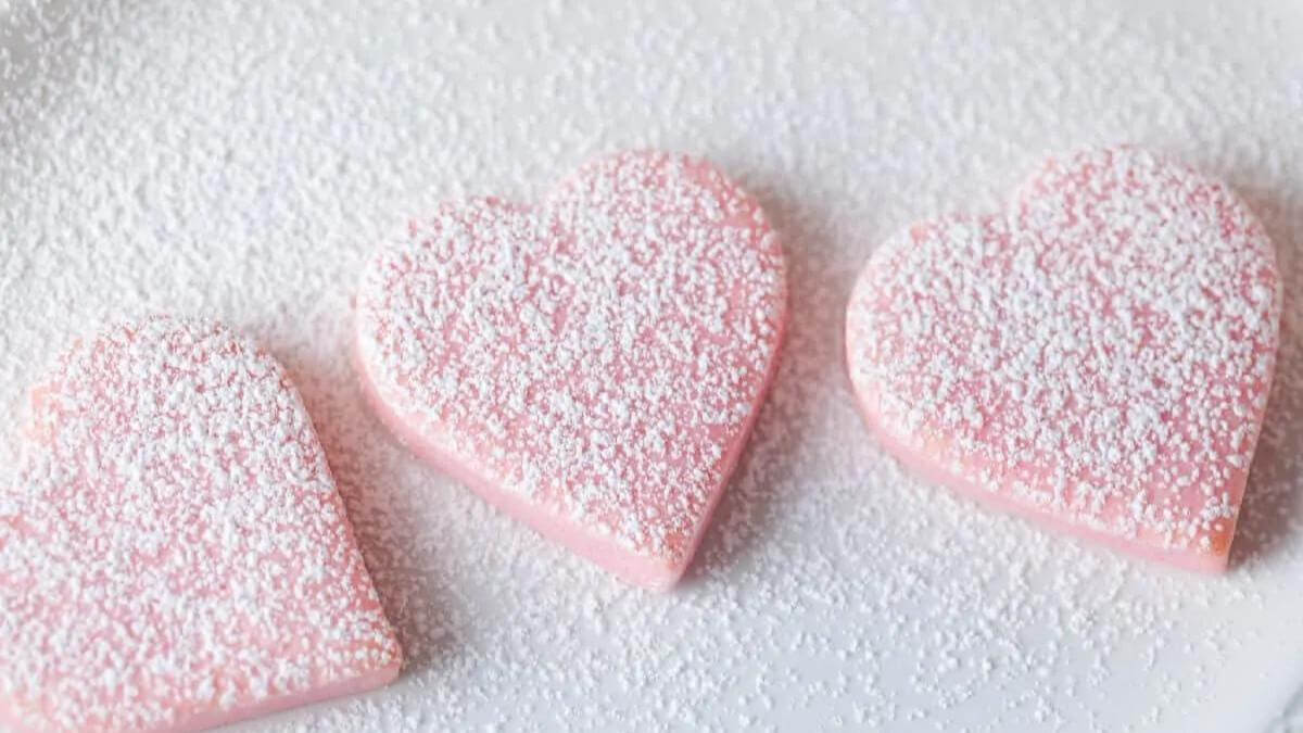 Three pink heart shaped cookies covered with powdered sugar.