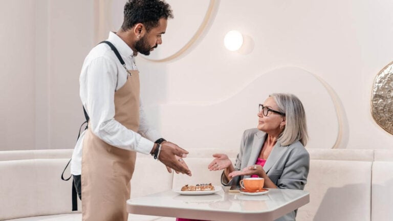 A woman talking to a waiter at a restaurant.