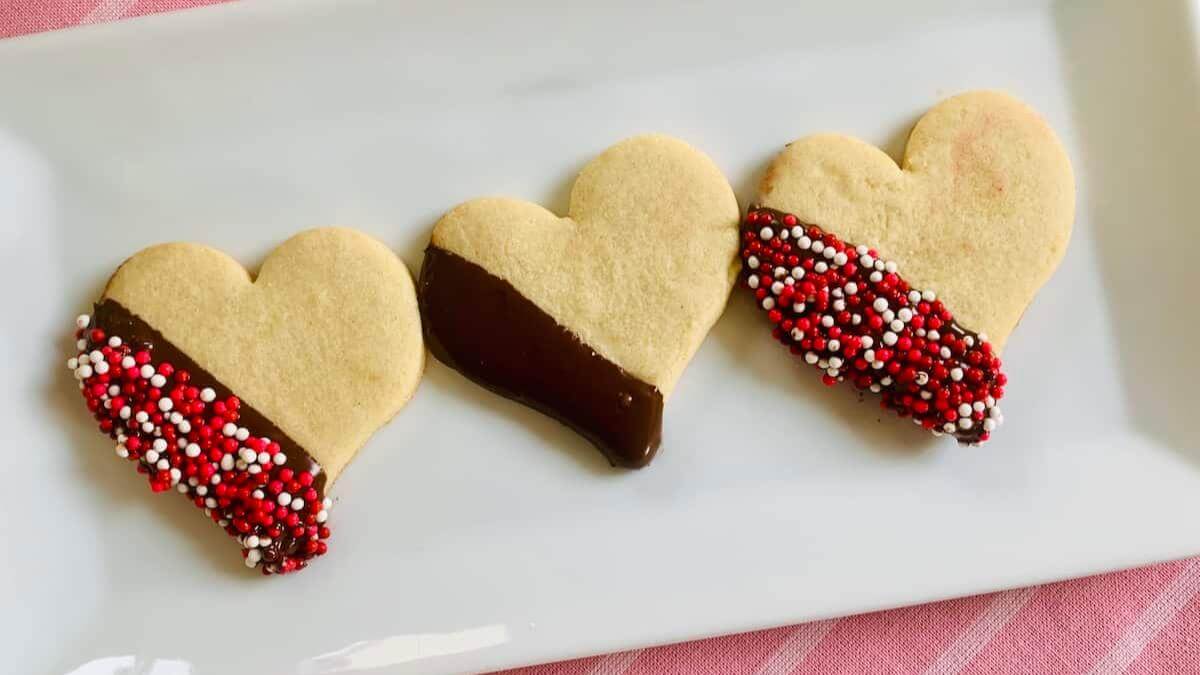 Three heart shaped cookies with chocolate and sprinkes.