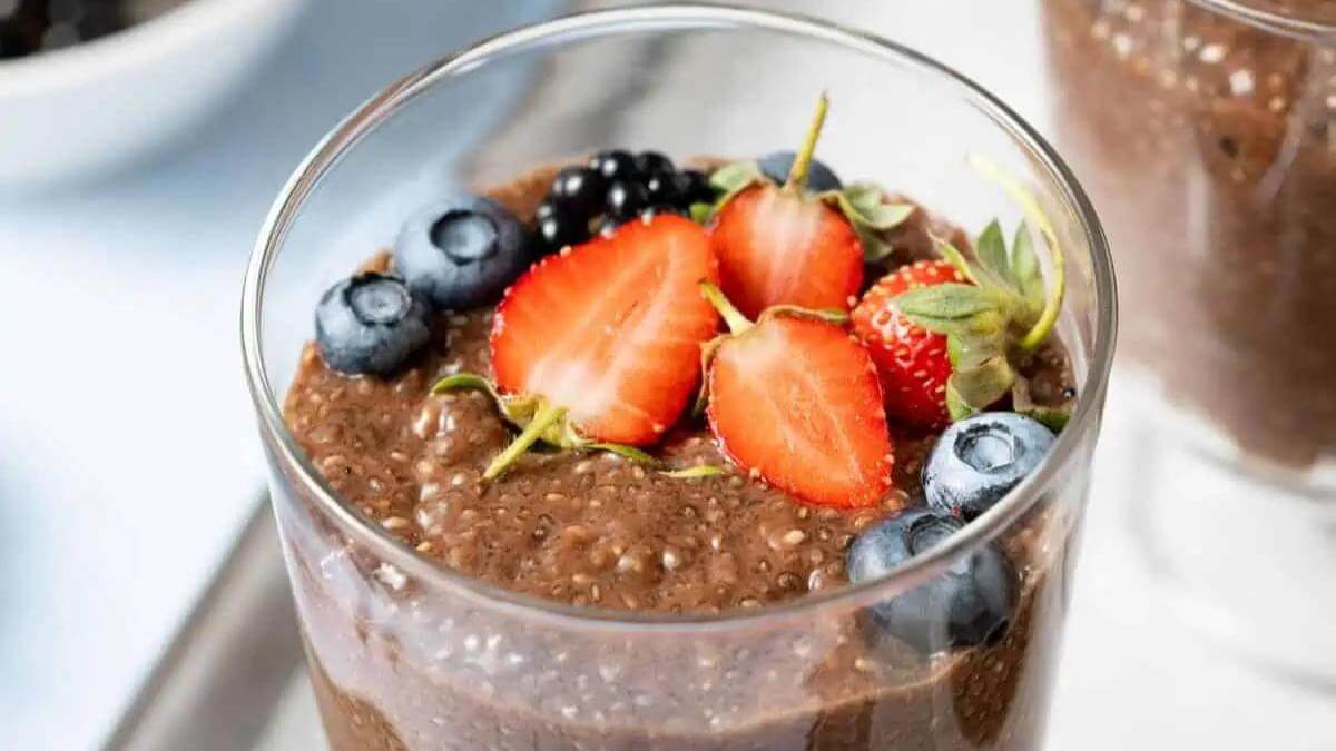 Chocolate chia seed pudding in a glass topped with strawberries and blueberries.
