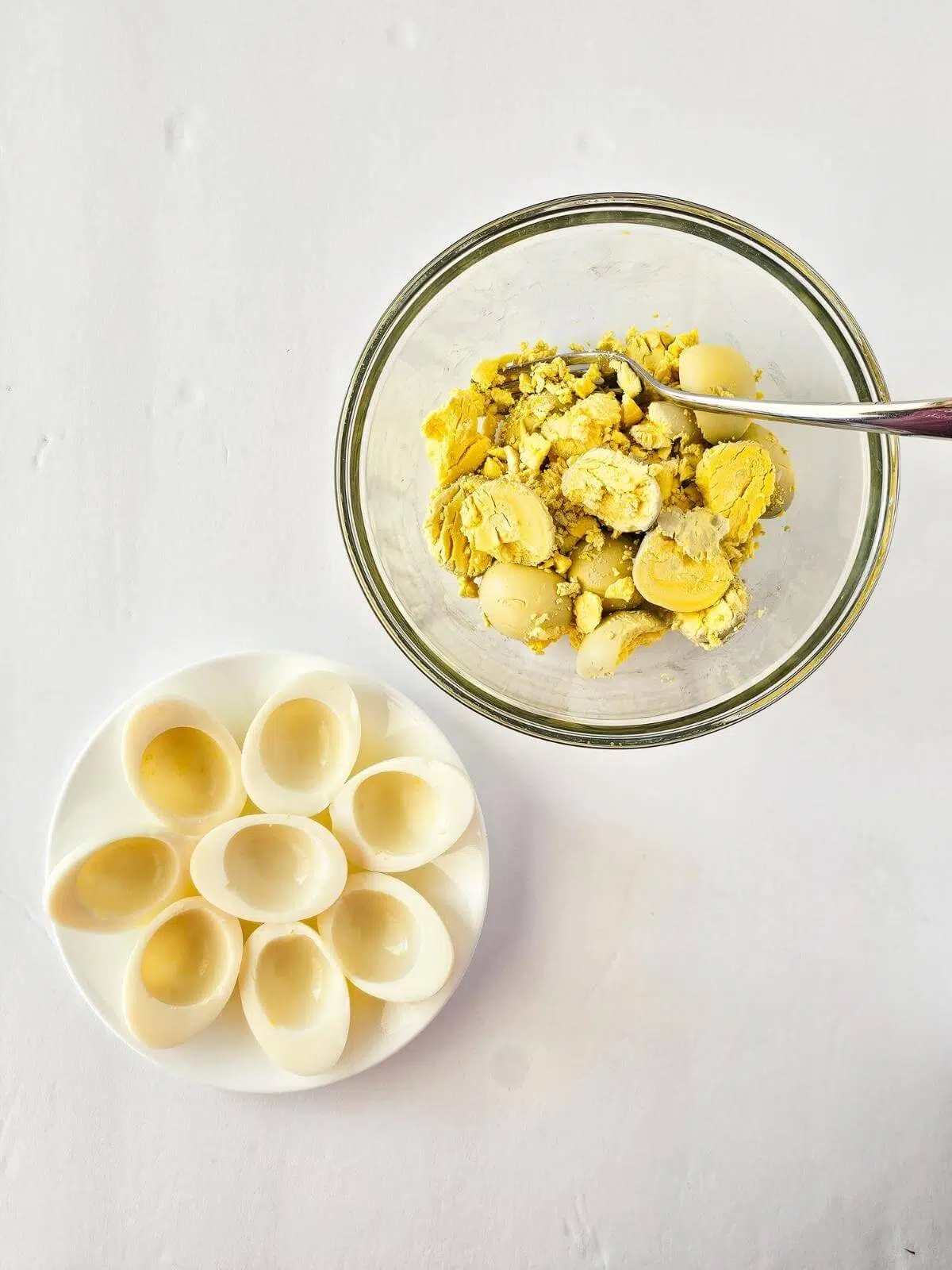 Egg yolks in a bowl next to a plate of hollowed out hard boiled eggs.