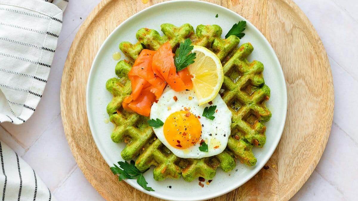 A spinach waffle topped with egg, tomato and lemon.
