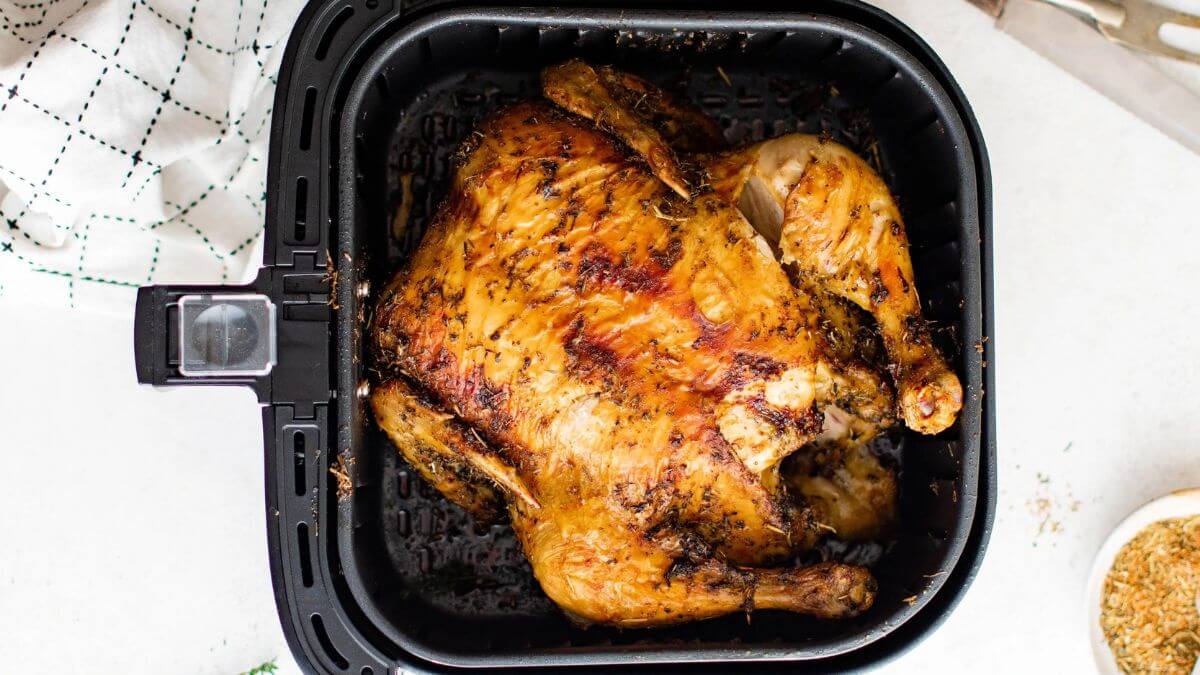 A cooked whole chicken in an air fryer basket.