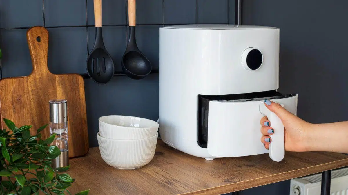 A hand holding the handle to an air fryer basket.