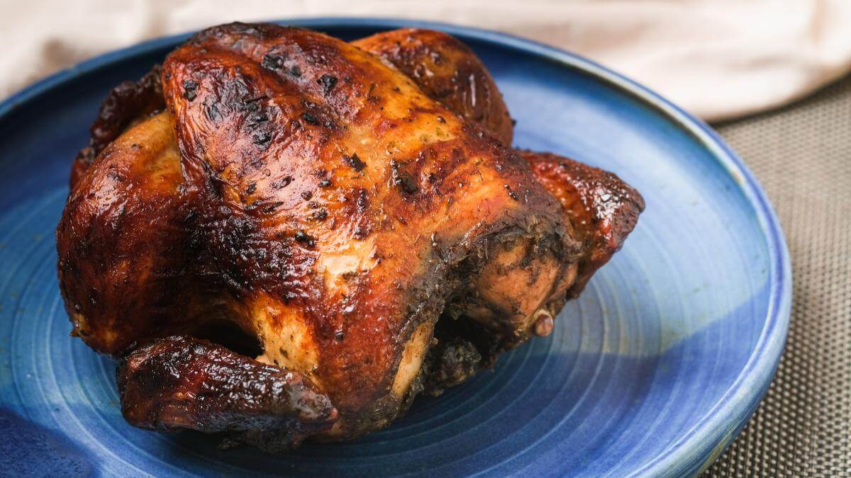 A whole cooked rotisserie chicken on a blue plate.