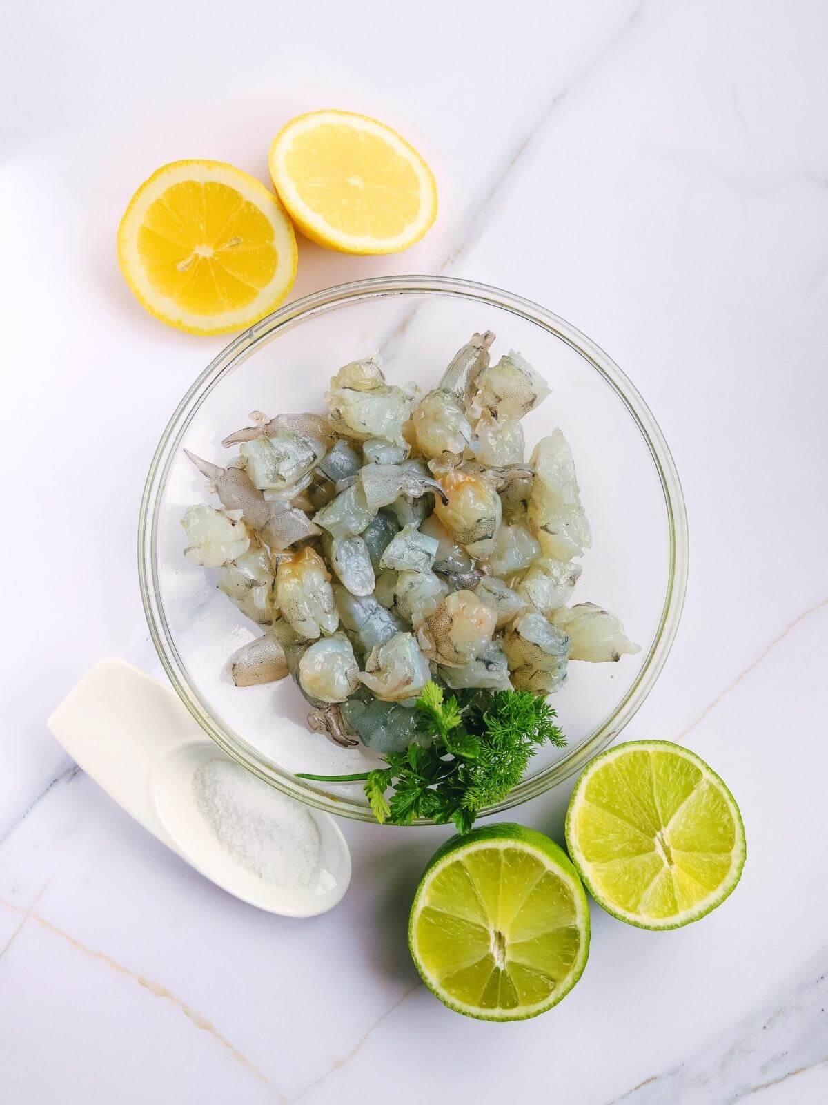 Raw shrimp in a bowl with lemons and limes.