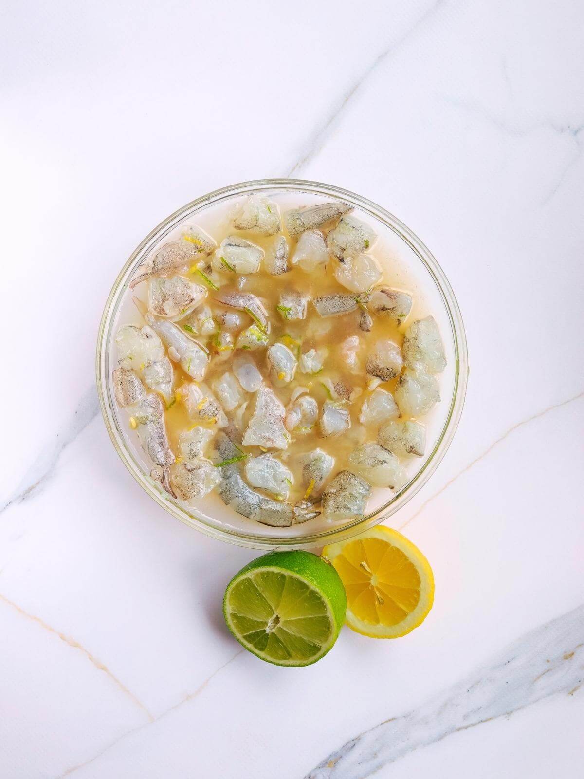 Raw shrimp marinating in lemon and lime juice in a bowl.