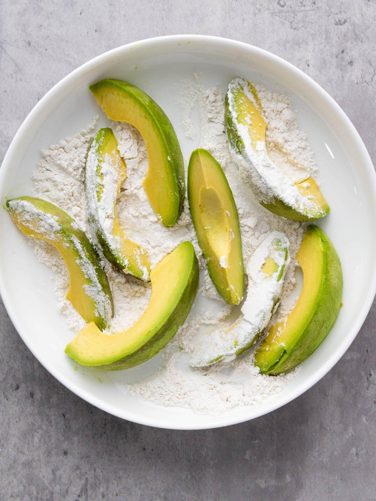 Sliced of avocado in a bowl of flour.