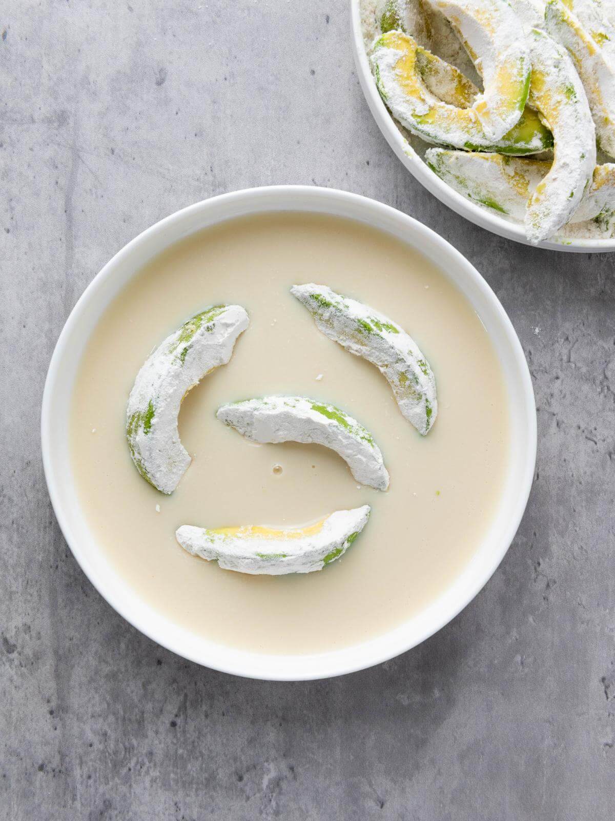 Avocado slices in a bowl of soy milk.