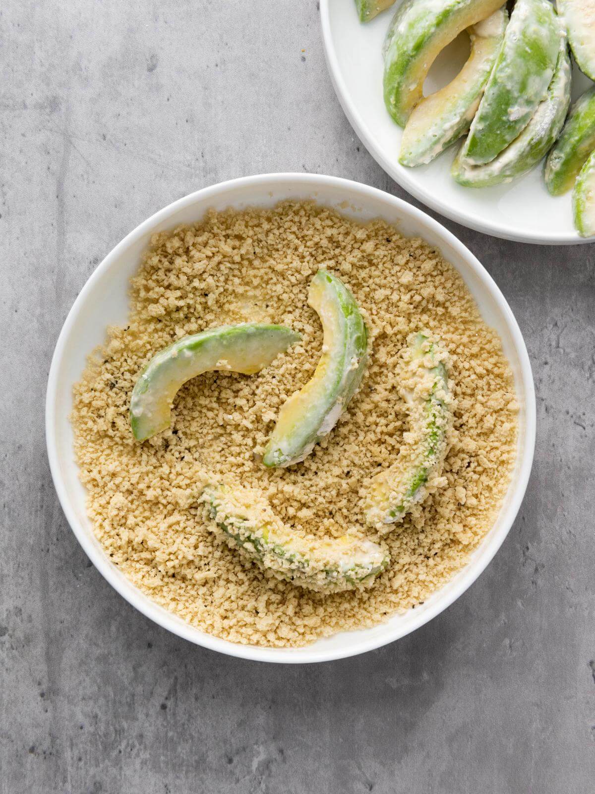 Avocado slices in a bowl of breadcrumbs.