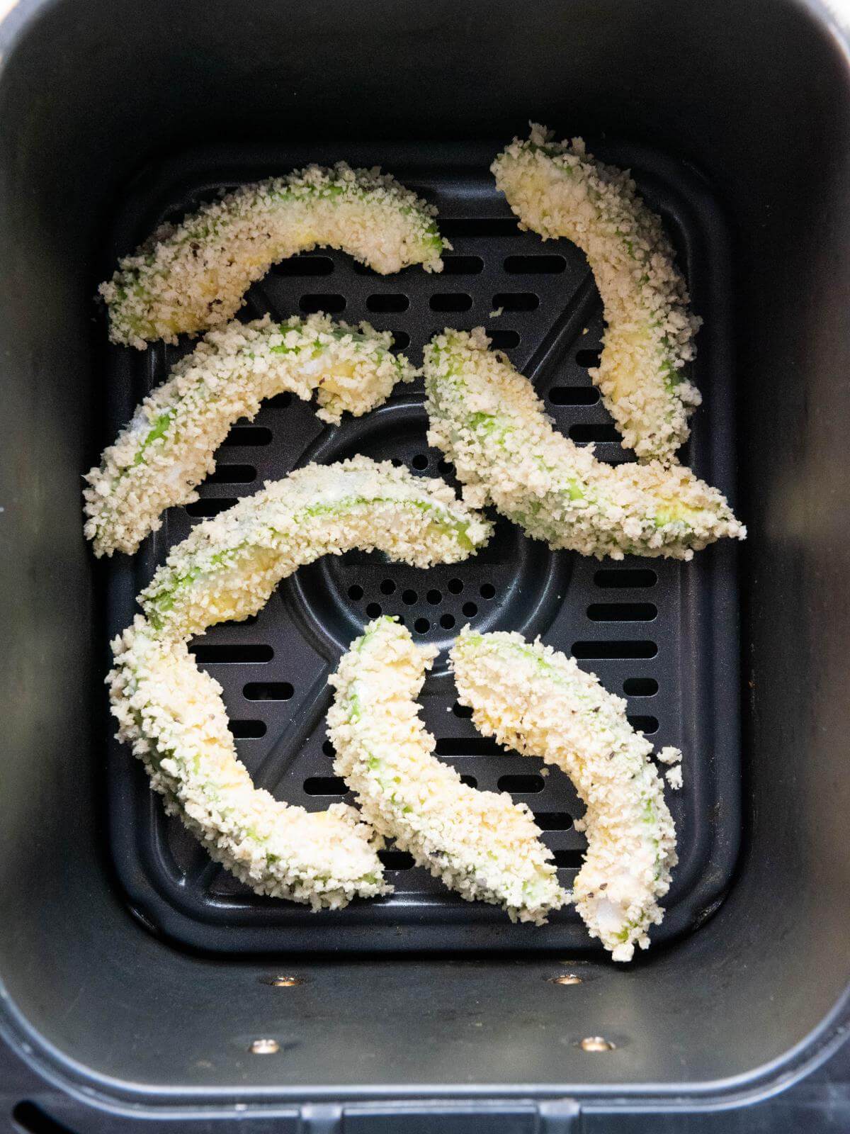 Breaded avocado slices in an air fryer basket.