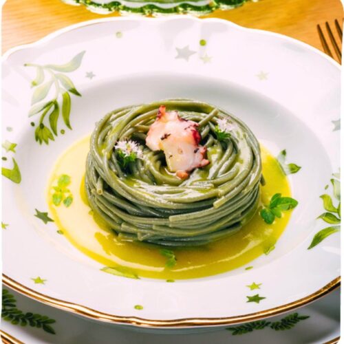 Green colored pasta on a plate with sauce.