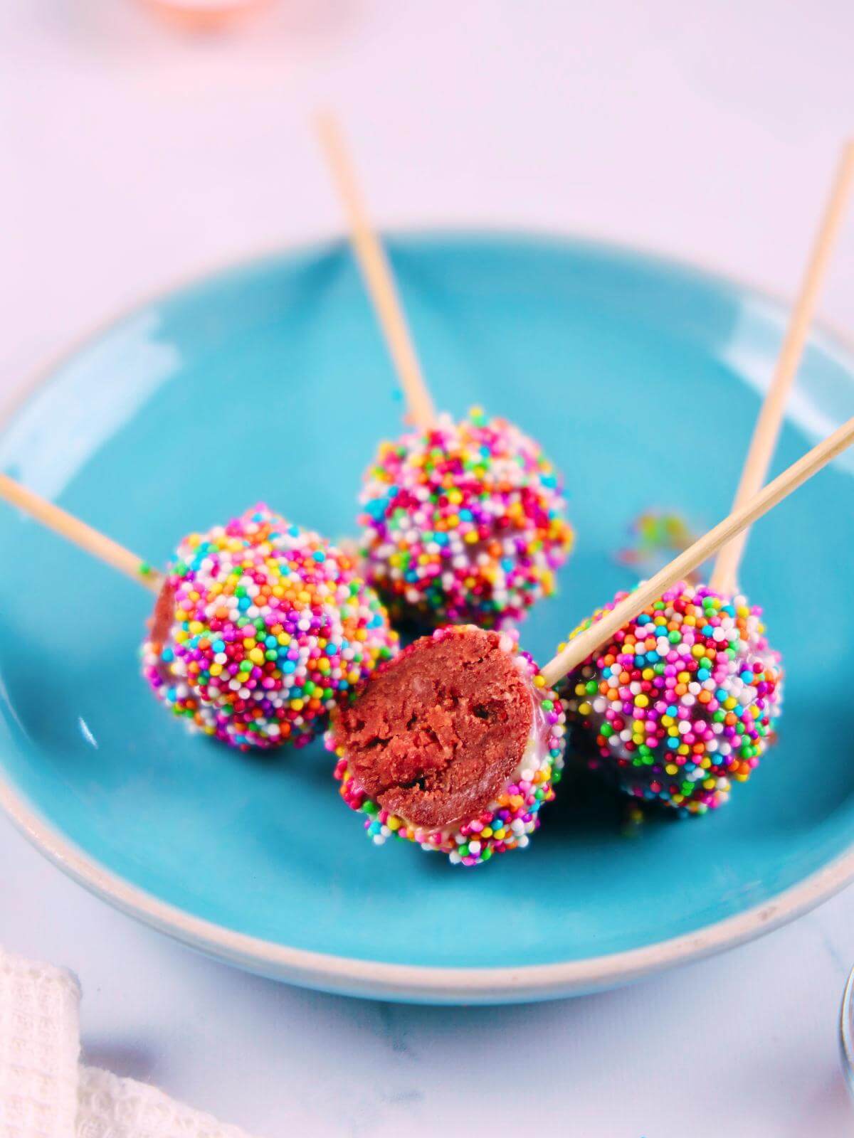 Four red velvet cake pops with colorful sprinkles.