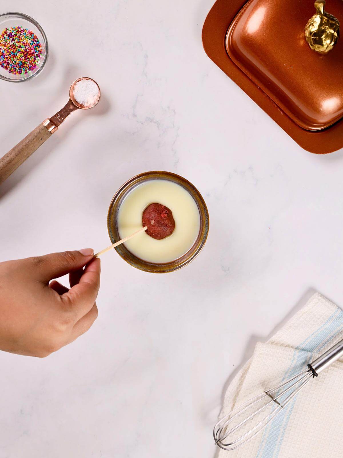 A hand dipping a cake pop into melted white chocloate.