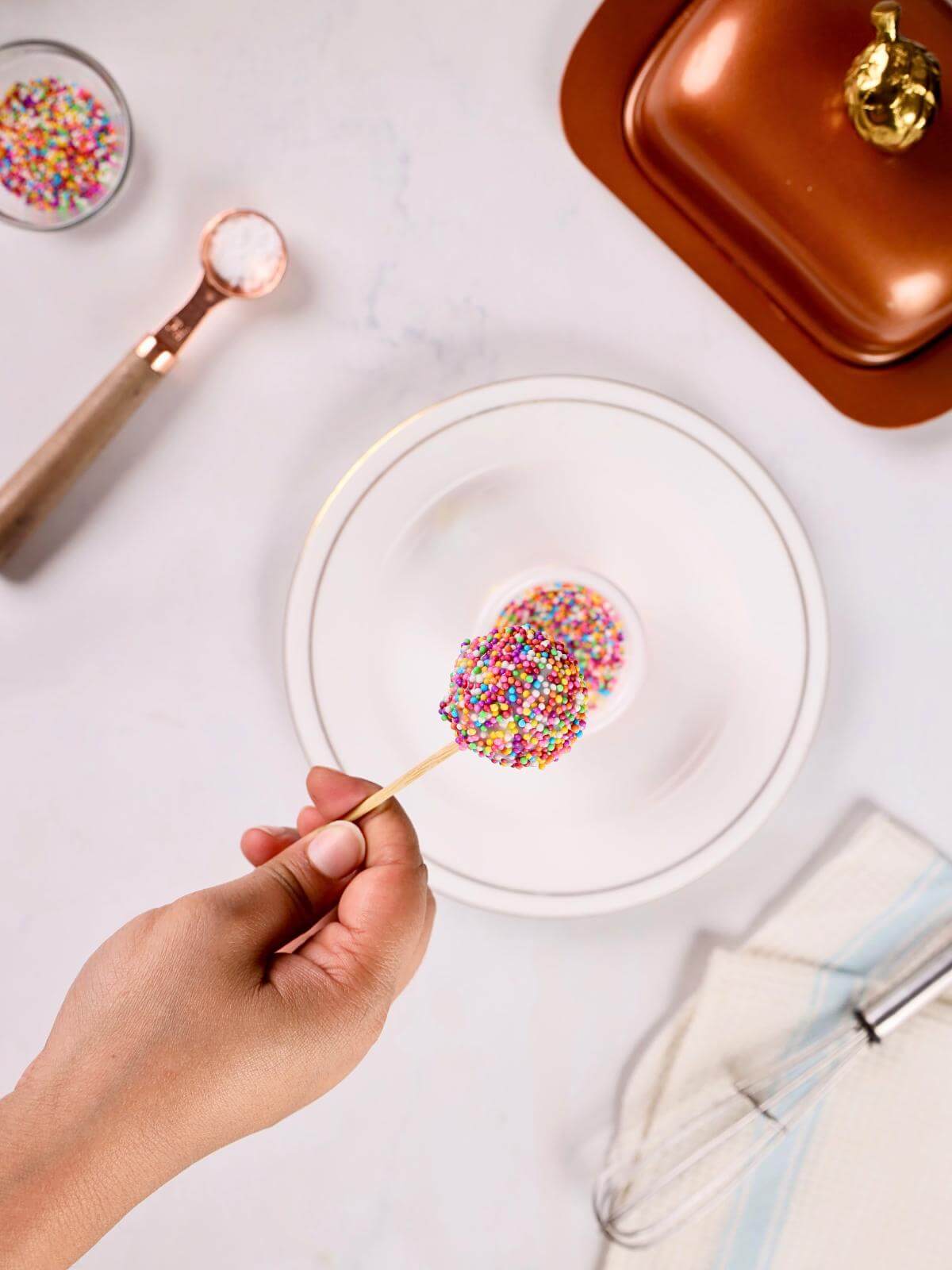 A hand dipping a cake pop into sprinkles.