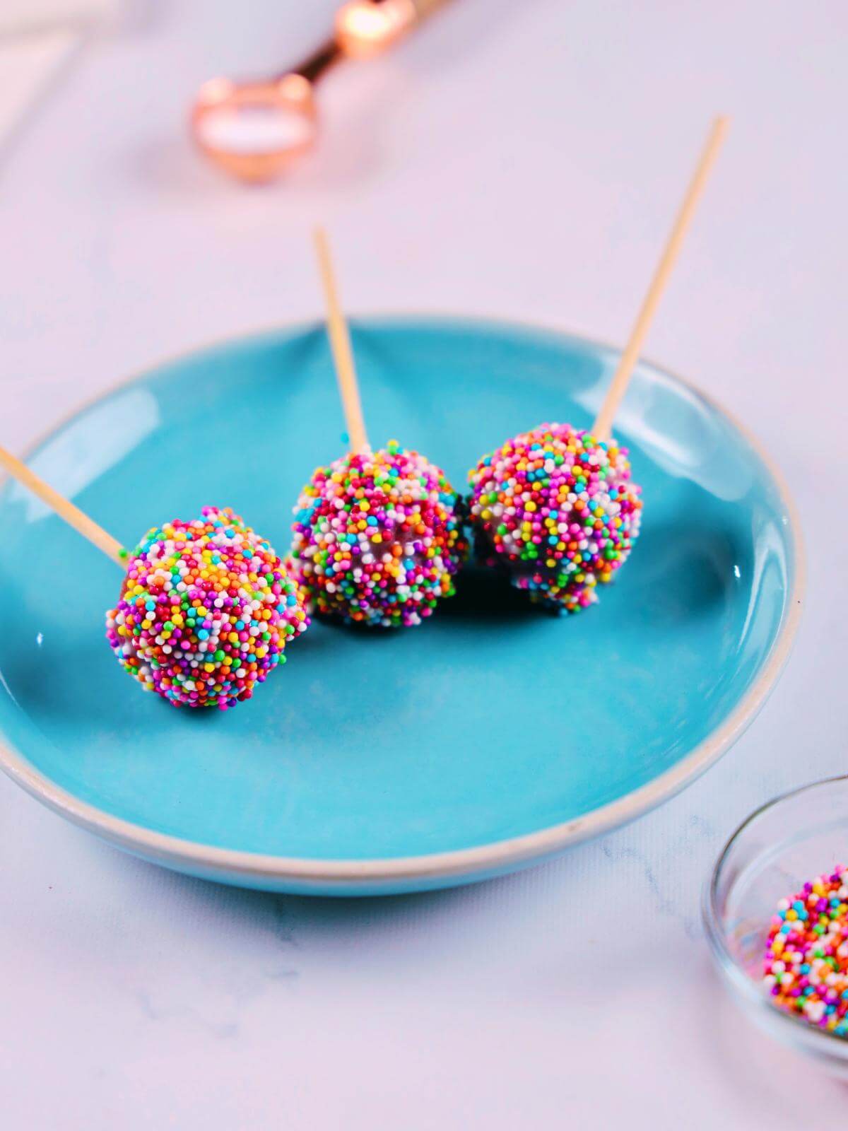 Three red velvet cake pops with colorful sprinkles.