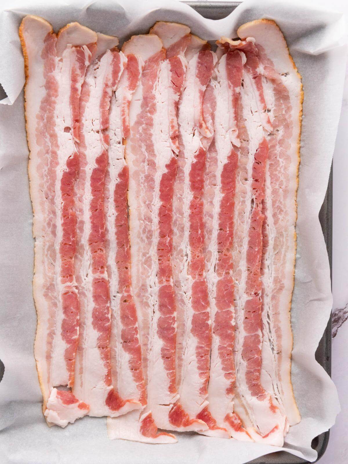 Raw bacon on a baking sheet.