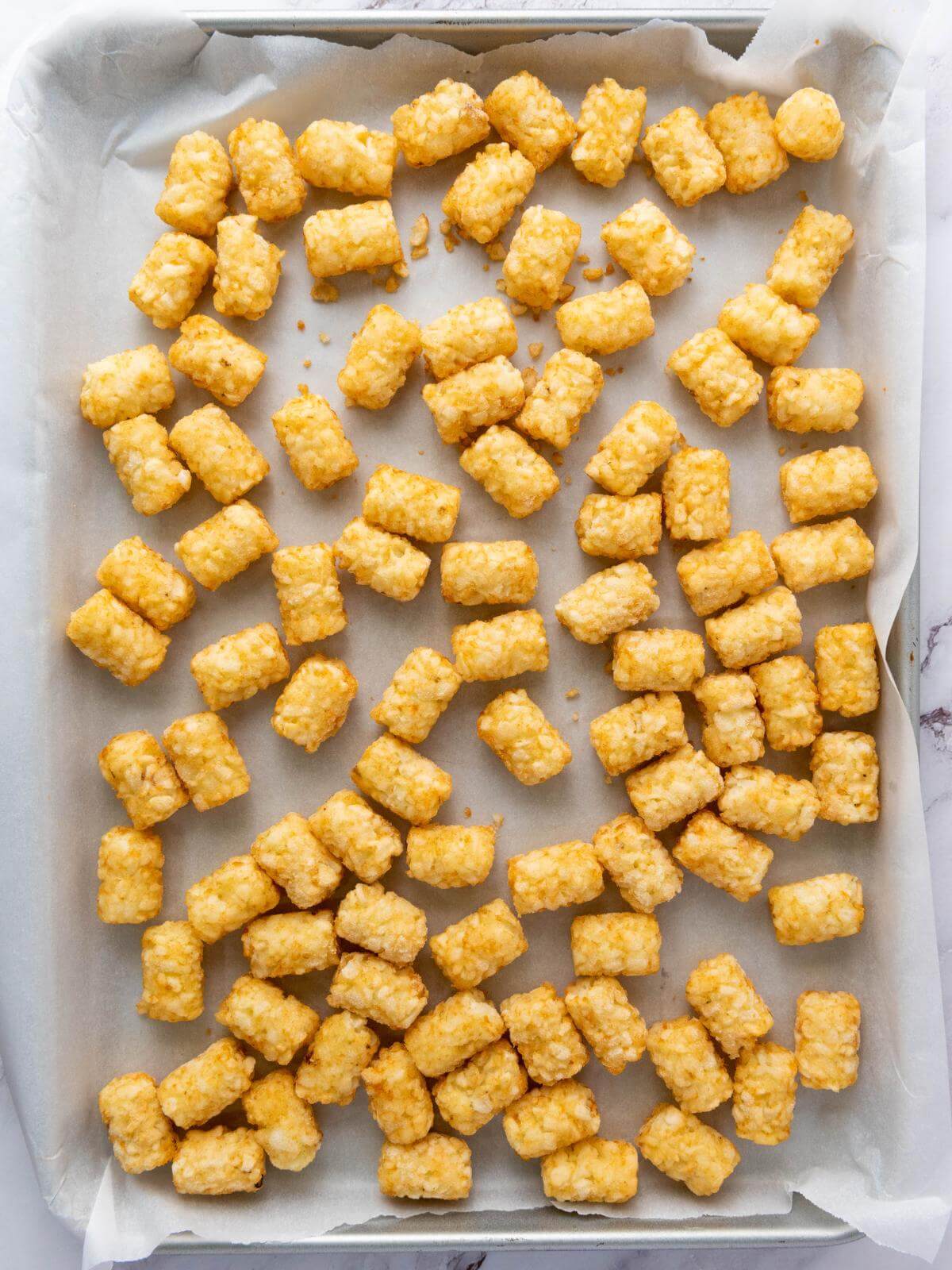 Raw tater tots on a baking sheet.