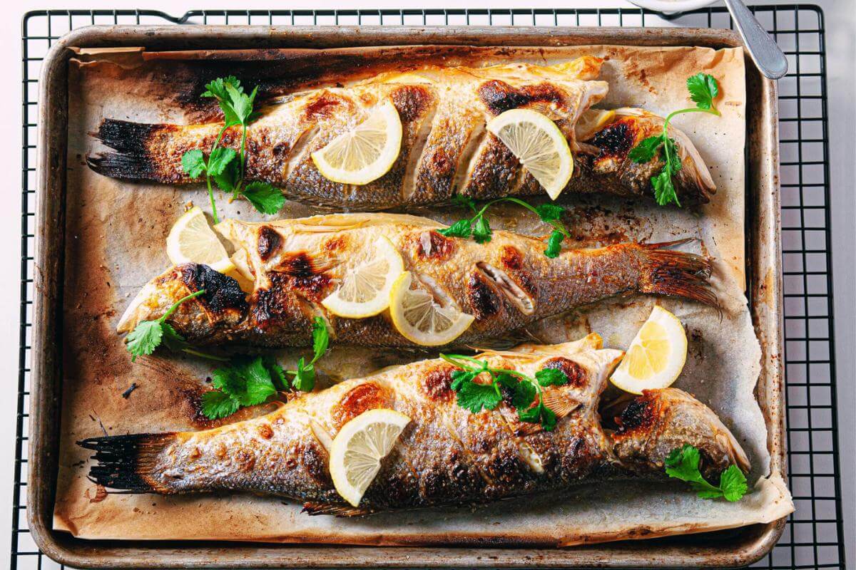 Whole cooked branzino fish on a tray.