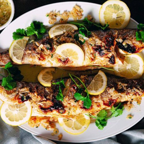 Whole cooked branzino fish on a plate.