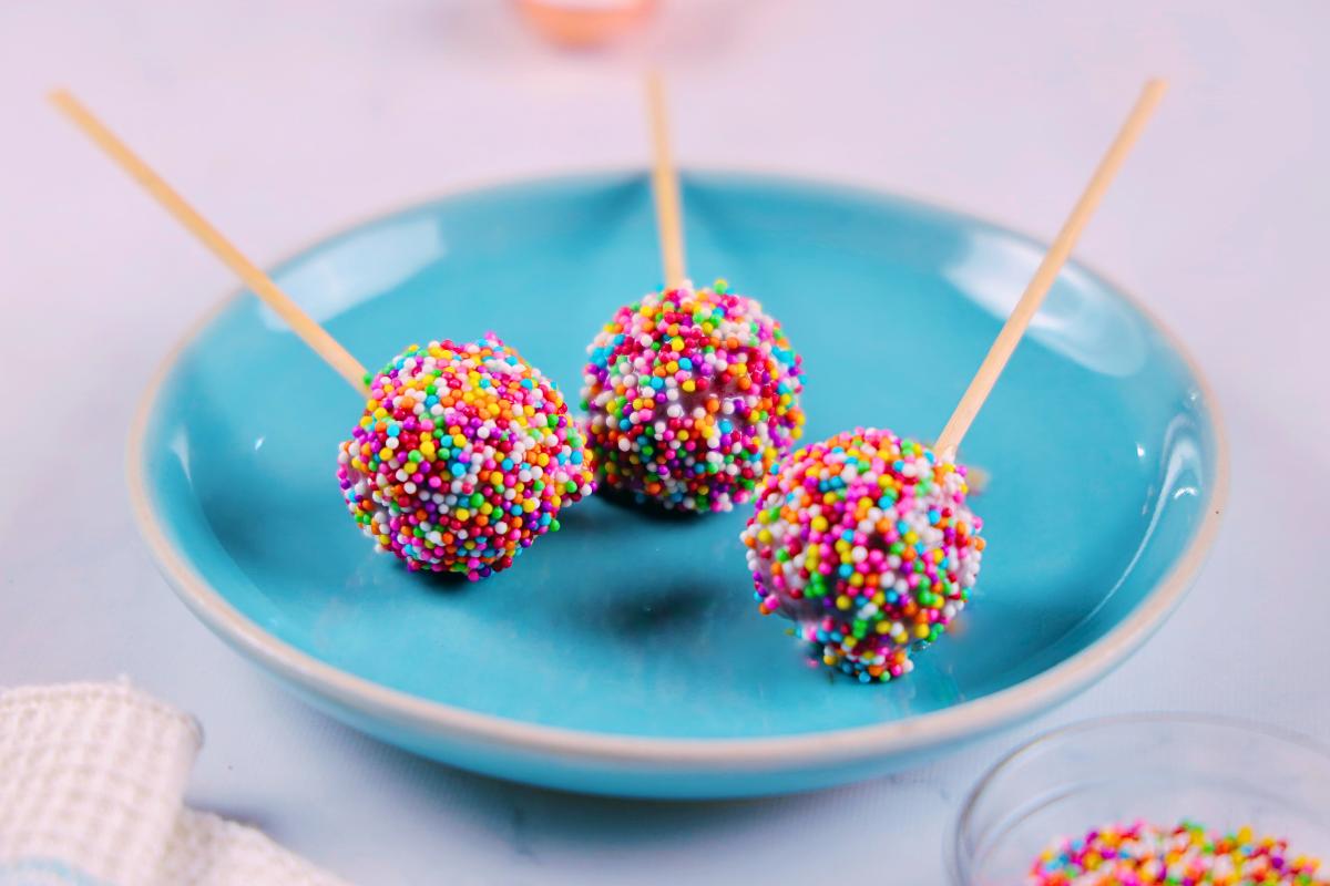 Three red velvet cake pops with colorful sprinkles.