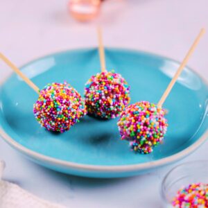 Three red velvet cake pops with colorful sprinkles.