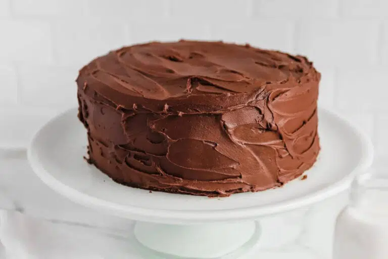 A frosted chocolate cake on a white serving dish.