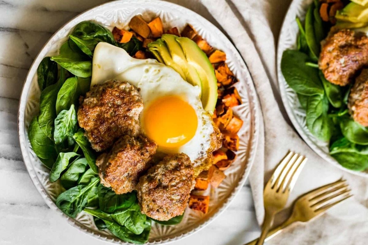 Turkey Breakfast Sausage on a bed of baby spinach with a side of Roasted Sweet Potatoes and topped with an over-easy egg and sliced avocado.