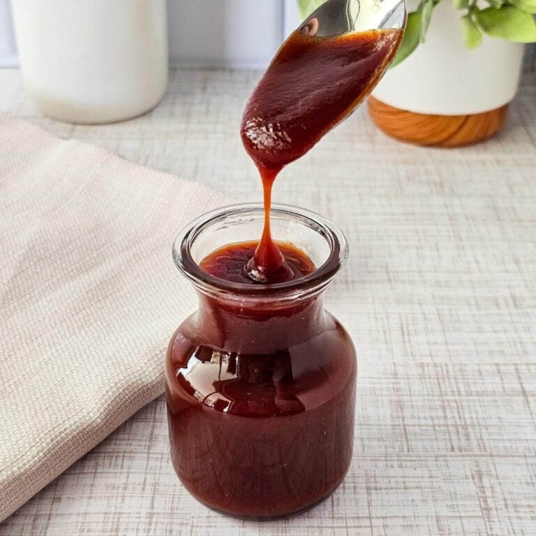 A spoonful of bbq sauce being dripped into a glass jar.