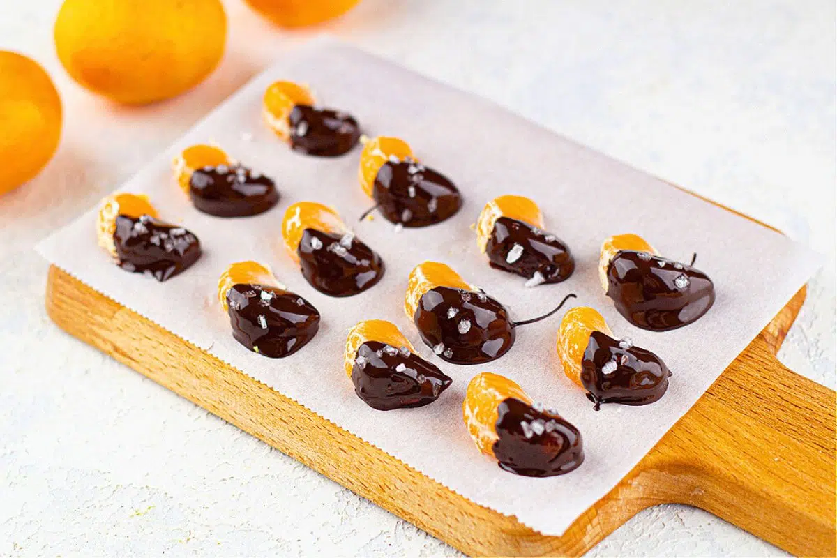Chocolate Dipped Mandarin Oranges with Flaky Sea Salt served on a wooden board.