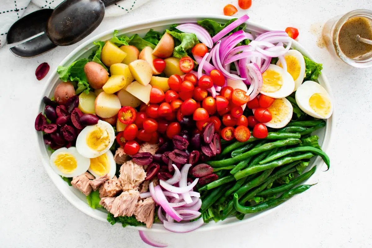 A bowl of Nicoise Salad alongside salad dressing.